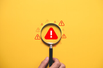 Warning alert concept with magnifying glass focusing on danger symbol over yellow background. Risk...