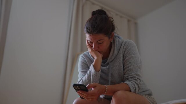 Fatigued woman sitting alone while scrolling on smartphone capturing emotional exhaustion, mental overload and disengaged everyday domestic life