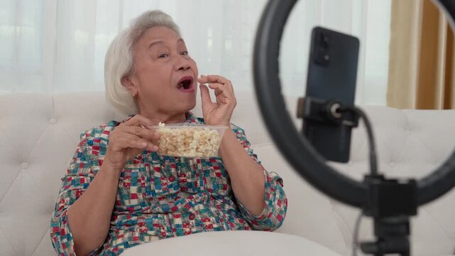 Popcorn and Content: An elderly woman, content and relaxed, enjoys popcorn while creating engaging content with a modern smartphone setup and ring light. A blend of leisure and digital interaction.