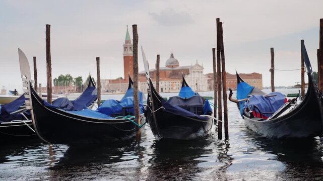 Gondolas moored at pier in Venice with San Giorgio Maggiore church background on cloudy day.