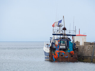 Naklejka premium Barco de pesca amarrado en el puerto de Barfleur, de color azul y rojo sobre el mar azul, viajando por la Normandía Francesa en verano de 2022