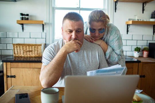 Couple reviewing household bills on laptop at kitchen table