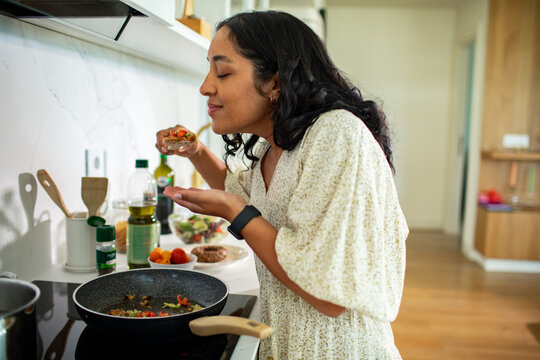 Young woman savoring aroma while cooking in home kitchen