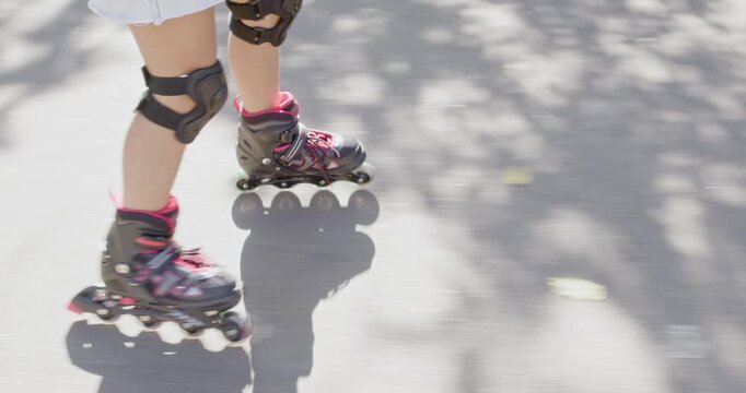 Girl glides forward on inline rollerblades across sunny park pavement. Child keeps knees soft moving feet with steady balance during sunny skating practice