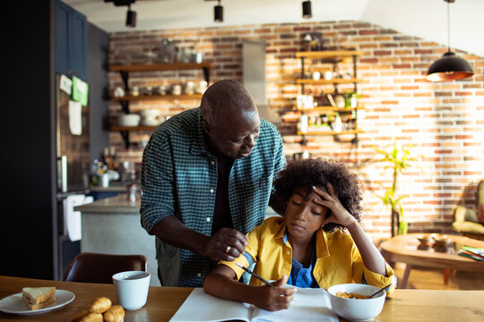 Father helping frustrated teen with homework at kitchen table