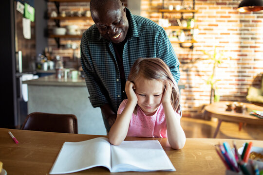 Supportive man helping frustrated girl with homework at home