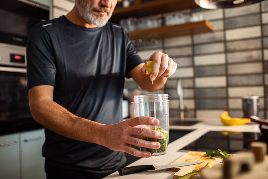 Mature man squeezing lemon into blender for green smoothie in home kitchen