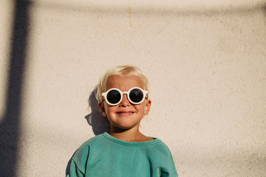 Smiling blond child wearing round sunglasses in warm sunlight.