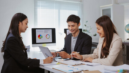 Diverse business professionals discussing financial reports and pie charts on laptops and monitors, working together at an office desk © amnaj
