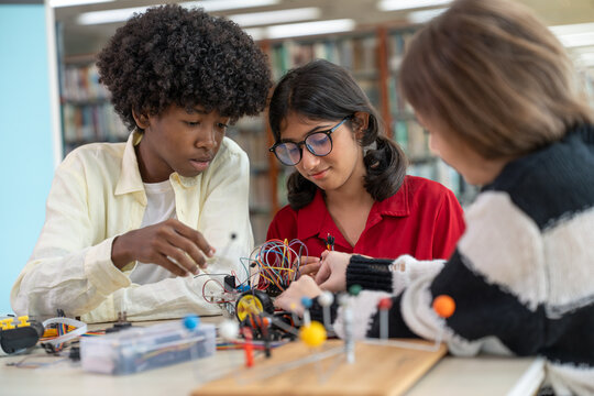 Diverse group of young student teenagers building robot kit together in school library. Multiethnic kids learning stem electronics engineering and robotics technology project