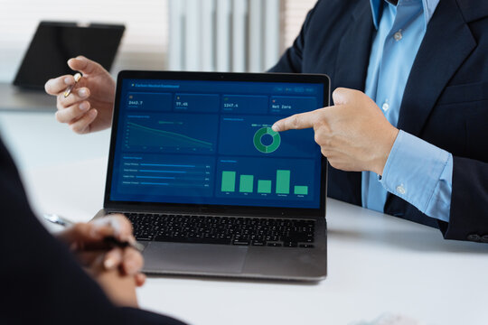 Business people collaborating, reviewing financial data dashboard on a laptop, discussing corporate strategy and sustainability performance