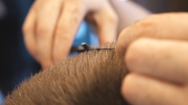 Close up arms of barber trimming brown hair of his client in salon. Male hands of hairdresser combing and cutting short hair of customer with hairbrush and scissors in barbershop. Slow motion