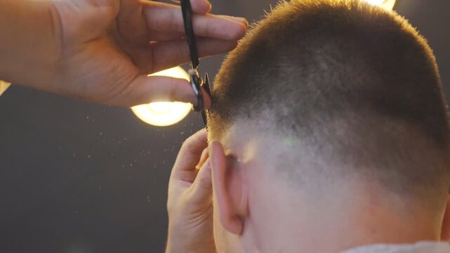 Male barber combing and cutting hair of customer by hairbrush and scissors in barbershop. Hands of hairdresser trimming hair of his client in salon. Hairstyling process. Low angle view Slow motion