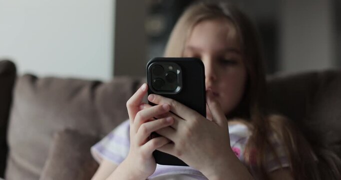 Caucasian kid girl scrolling typing screen playing games online using mobile phone telephone application. Device overuse.