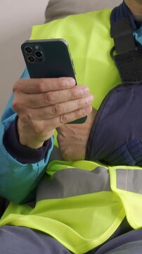Close up of repairman hands with broken arm wearing sling using smart phone at home