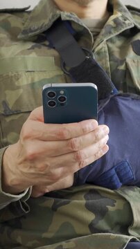 Close up of soldier hand with broken arm wearing sling using smart phone at home