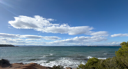 Fototapeta premium Rocky coastal view of the Aegean Sea under bright clouds near Vouliagmeni in Attica Greece