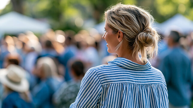 Rear view of a woman smiling and participating in a community gathering outdoors on a sunny afternoon, community event concept, outdoor community photography, social inclusion