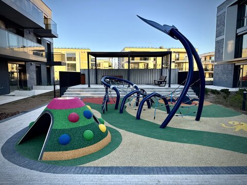 Modern children's playground in Vilnius features a variety of innovative structures. A colorful dome-shaped climbing structure with polka dots sits alongside blue, arching metal elements forming a cli
