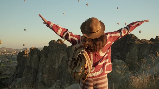 Inspired woman traveler spreads her arms in admiration as she watches hot air balloons fly in Cappadocia, T&uuml;rkiye