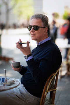 Senior man sitting at table at sidewalk cafe and using a cellphone