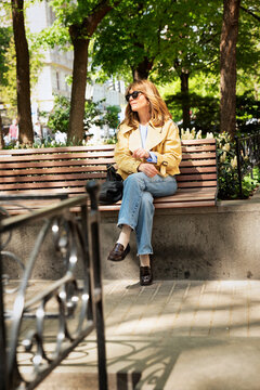 Smiling middle-aged woman sitting in a city park and using a smartphone
