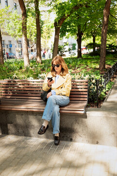 Smiling middle-aged woman sitting in a city park and using a smartphone