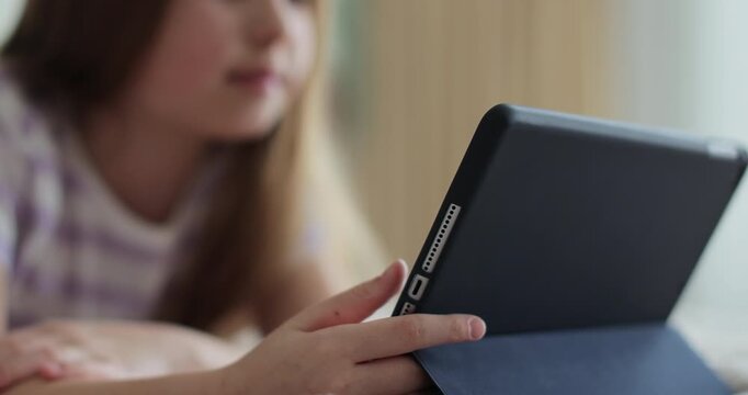 Kid girl in bed playing a tablet in social internet. Close up of little girl watching video on the digital tablet. The problem of addiction to gadgets.