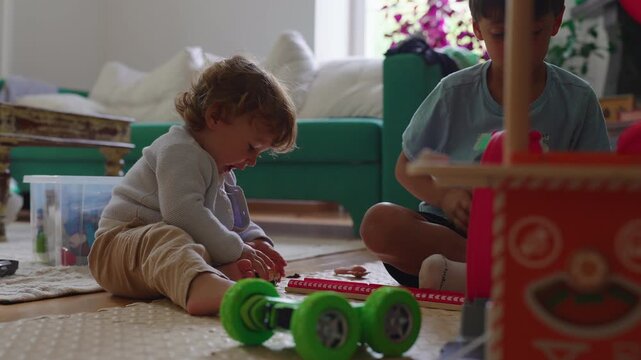 Toddler sitting beside older brother while examining toy car during indoor playtime capturing sibling bonding, curiosity and authentic childhood learning at home