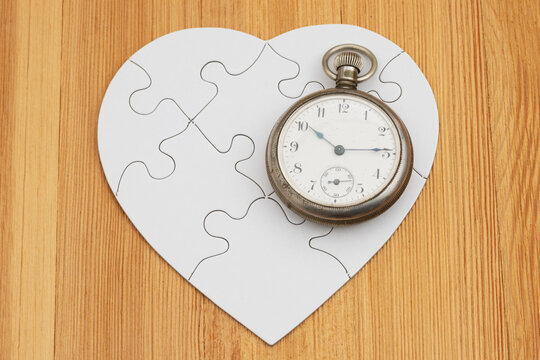 Blank white puzzle heart with antique pocket watch on wood for time to heal