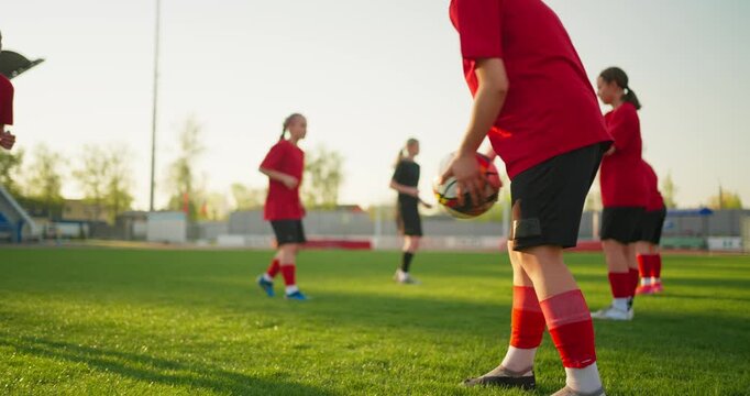 Youth soccer players in red uniforms practice ball control drills on a sunny grass field during team training at an outdoor stadium