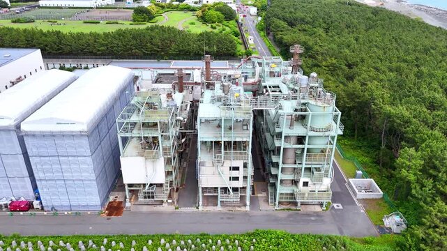 Aerial video showcasing a massive industrial processing plant surrounded by a lush green coastal forest. A great visual metaphor for the relationship between modern industry, infrastructure, and the e