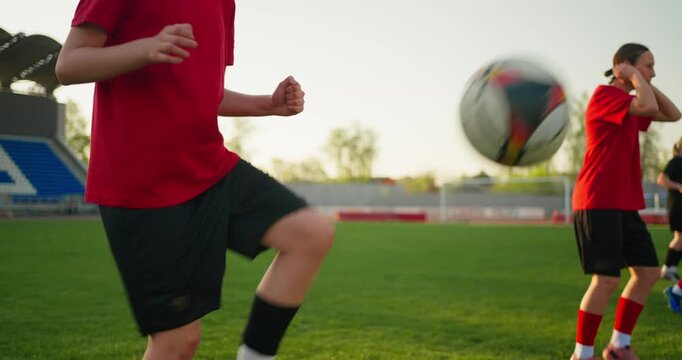 Young soccer players in red jerseys warming up on a sunlit grass field during team practice, with focus on athletic movement and training