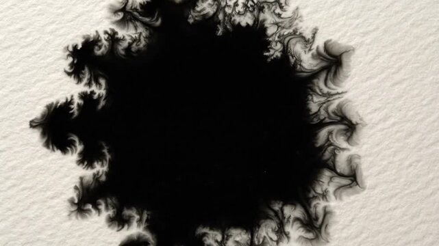 Black ink drop spreading on white textured paper creating a beautiful organic shape