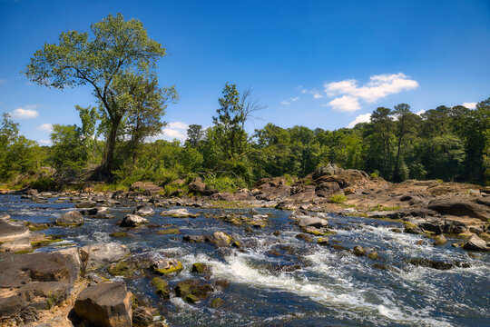 A beautiful landscape under a blue sky of an American river in the mountains of Pittsboro, North Carolina with lots of rocks and bubbly whitewater rapids.
