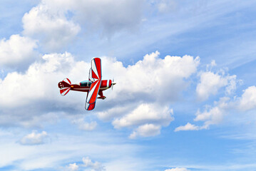 A red aerobatic biplane performing air shows in a blue sky with white clouds. Classic airplanes © Toni