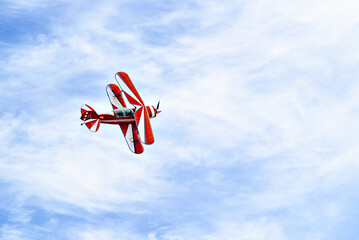 A red aerobatic biplane performing air shows in a blue sky with white clouds. Classic airplanes  © Toni