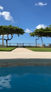 Vertical tracking shot of a luxury beachfront resort in Costa Rica featuring swimming pool, tropical trees and ocean views under a bright blue sky. Relaxing vacation atmosphere with serene coastal sce