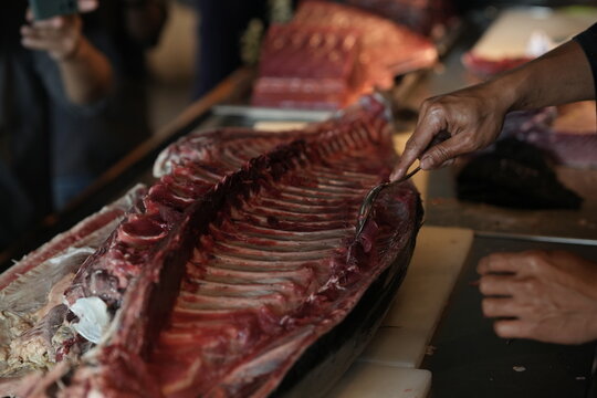 Fresh tuna being filleted by hand with knife, raw seafood cutting process in traditional market food photography