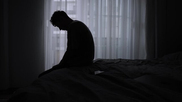 Young man sitting alone in the dark after messaging, feeling ignored and ghosted. Concept of digital heartbreak and loneliness online