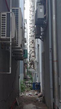 Urban alleyway running between tall buildings. Featuring rows of stacked air conditioning units. Exposed pipes. And debris on the ground. Illustrating dense city development and hidden infrastructure