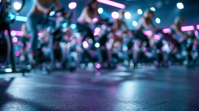Blurred indoor cycling class with blue magenta neon lights glossy floor and exercise bikes for fitness background use