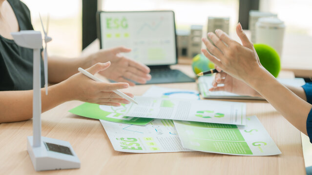 Business team discussing ESG investment and green business development strategies in office.Group of colleagues analyzing ecological data and sustainable goals report on digital tablet
