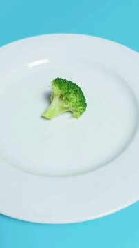 Dieting and healthy eating concepts with a single small broccoli floret on a white plate against a vibrant blue background, symbolizing minimal portions and wellness programs