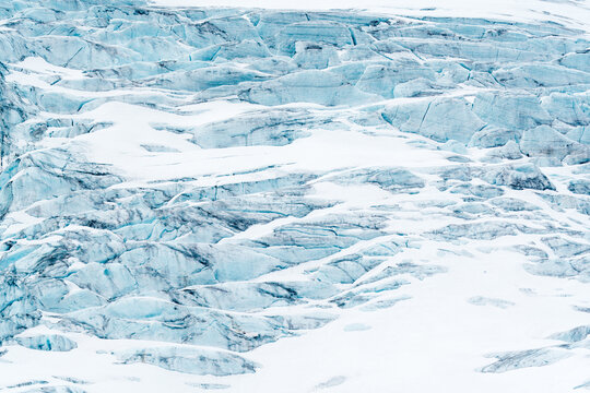 View of the textured surface of a massive glacier with deep blue crevasses and layers of white snow Svalbard and Jan Mayen.