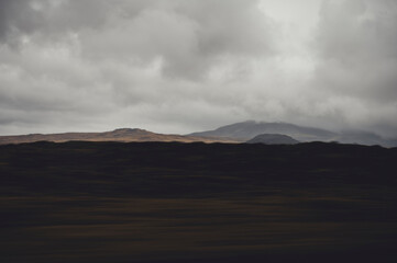 Fototapeta premium Dark volcanic landscape of Iceland with distant hills under dramatic overcast sky