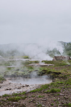 Geothermal hot spring pool with steam and traditional turf roof hut in rural Iceland