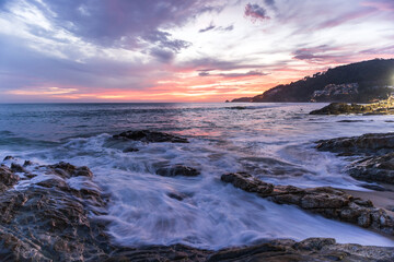 Obraz premium Rocky shoreline during vibrant twilight sunset over the ocean waves