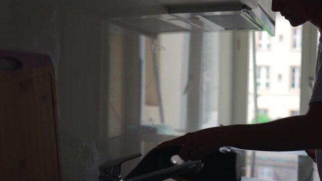 Woman wiping kitchen wall with electric cleaning device after steam treatment capturing domestic hygiene, surface maintenance and realistic home cleaning routine