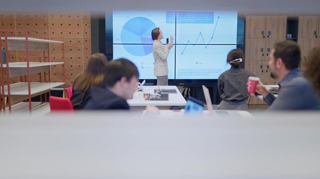 A businesswoman delivers a compelling presentation on data analysis to her team. Coworkers attentively listen, engaging in the modern office meeting.